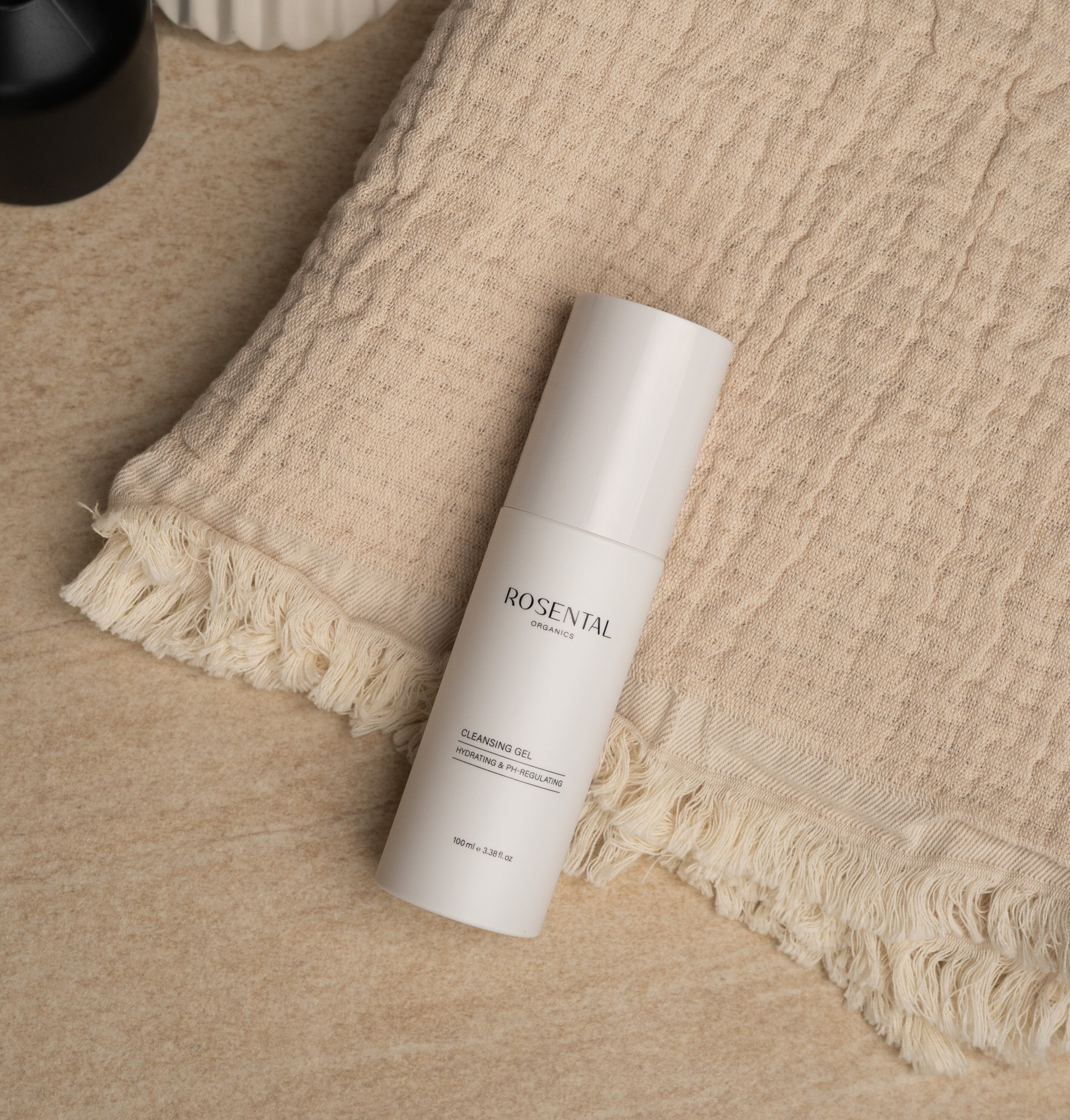 Cleansing Gel in beigefarbener Verpackung, welches stilvoll platziert auf einem Handtuch liegt, das sich auf einer glatten Marmoroberfläche befindet.