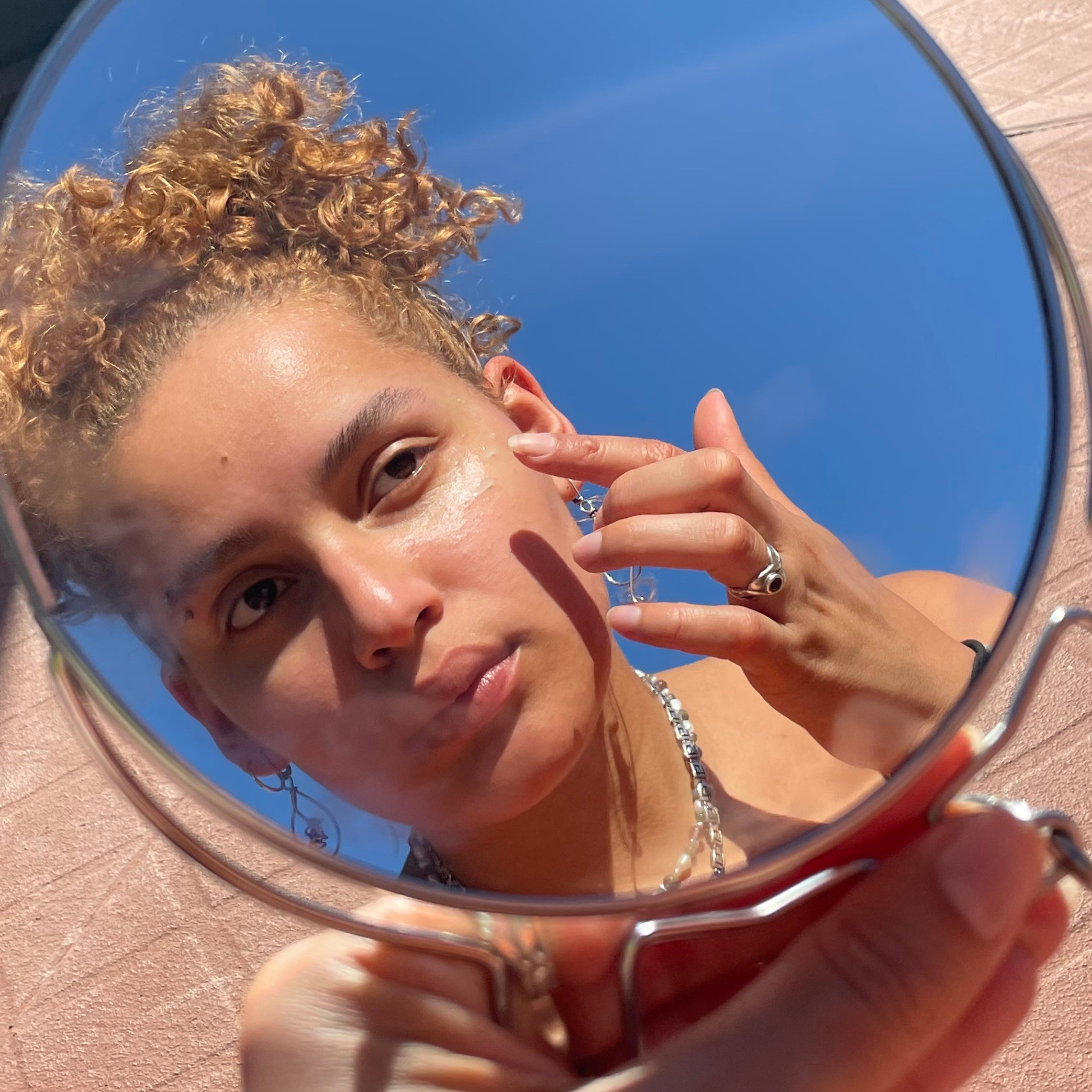 Das Spiegelbild einer Frau, welches ein Produkt von Rosental Organics auf ihr Gesicht aufträgt.